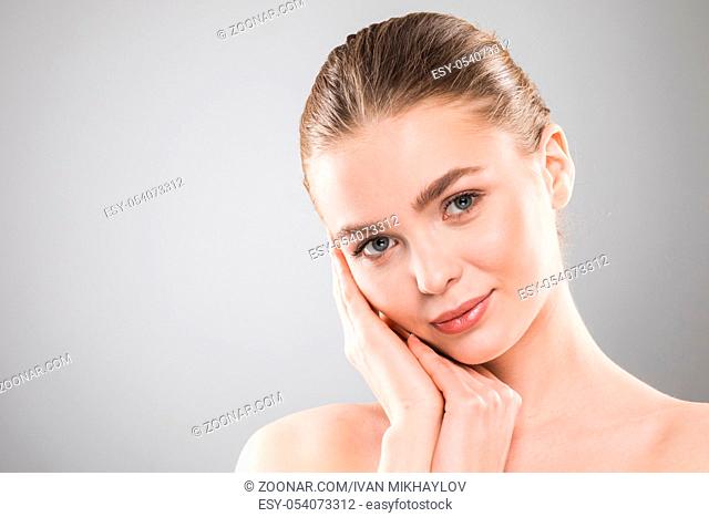 Beautiful young woman with clean fresh skin touch own face . Facial treatment , cosmetology , beauty and spa