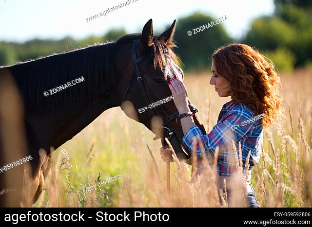 Young woman and horse in the meadow at summer evening, telephoto