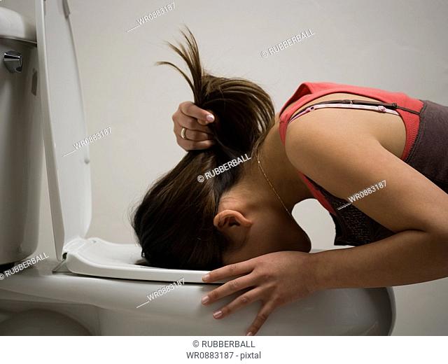 Profile of a young woman vomiting into a toilet bowl