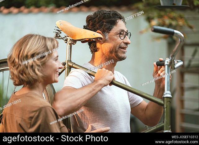 Mature woman with man carrying bicycle on shoulder