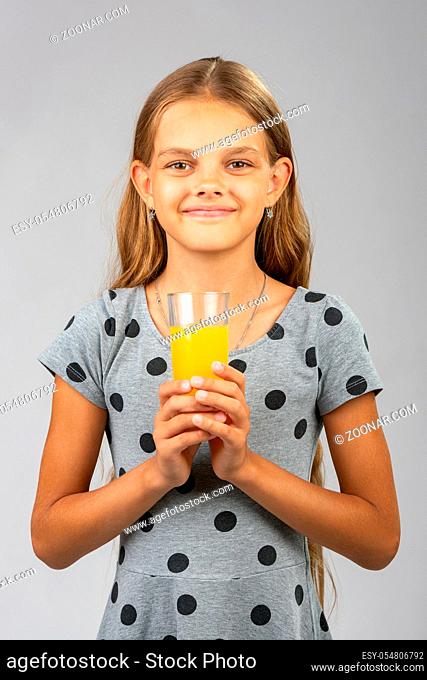 A girl holds a glass of juice in her hands with both hands