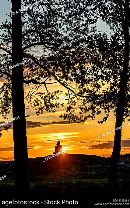 Stockholm, Sweden A person sits on a rock formation looking at the setting sun