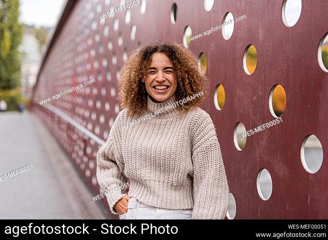 Cheerful young blond woman standing against metallic wall