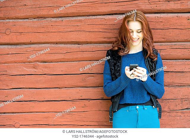 Beatiful young woman with red hair smiling and looking at her mobile phone