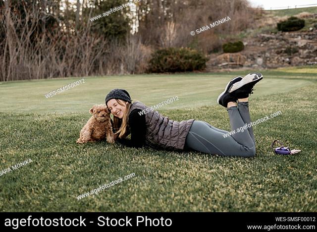 Smiling woman with poodle lying on grassy land in park