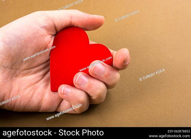 Red color heart shaped object in hand on dotted paper