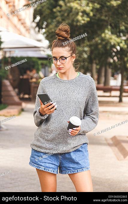 Young girl dressed in casual clothes with phone and a cup of takeaway coffee. Daily life of youth. People online