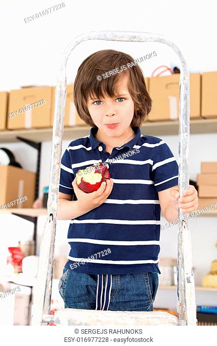 Cute, adorable boy eating apple on a stepladder