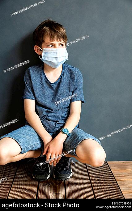 Young boy sitting against a wall wearing a protective mask during Covid-19 pandemic