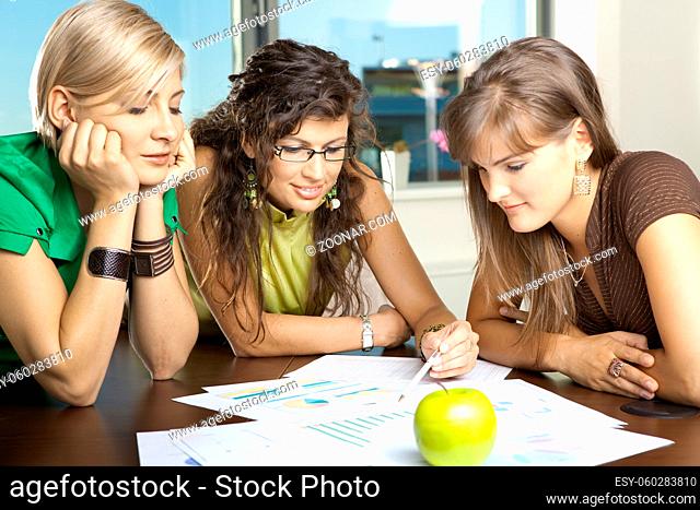 Casual businesswomen leaning on table in meeting room, discussing finacial charts