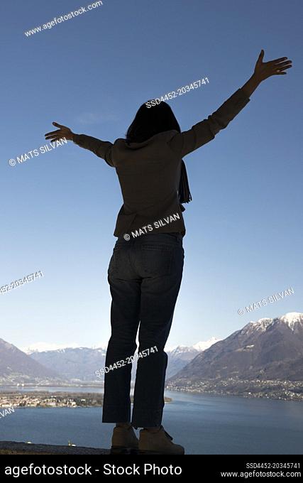 Woman with Arms Outstretched and Enjoy the Panoramic View over Alpine Lake Maggiore with Snow-capped Mountain in Ascona, Switzerland