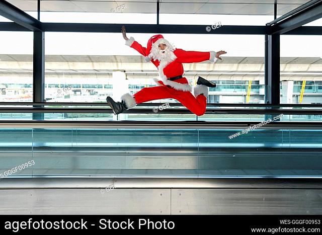 Man wearing Santa Claus costume jumping on moving walkway at airport