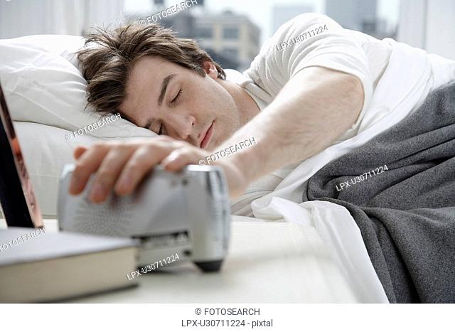 Young man switching alarm clock off