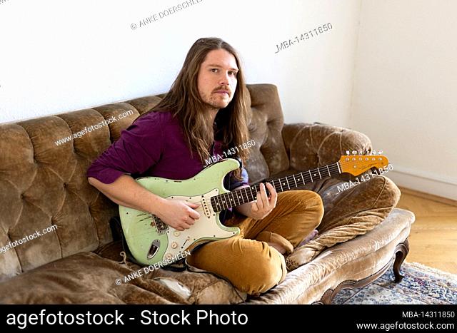 Man sitting on a sofa and playing guitar