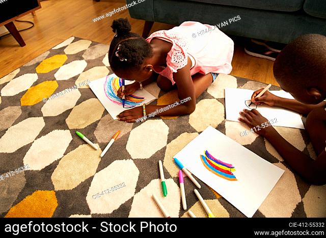 Girl drawing multicolor rainbow with markers on living room rug
