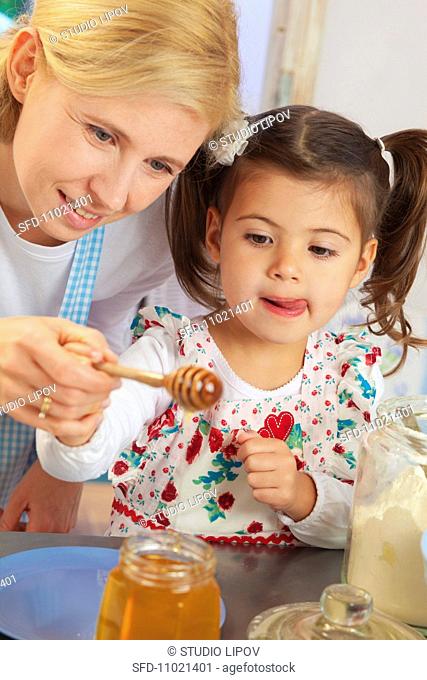A mother and daughter holding a honey spoon over a jar of honey