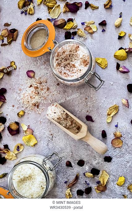 High angle close up of dried flower petals scattered around wooden spoon and glass jars with coarse salt