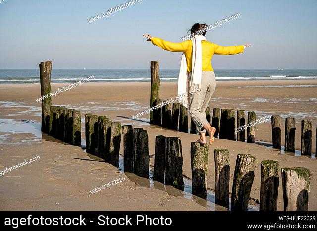 Mature woman with arms outstretched balancing on wooden posts at beach