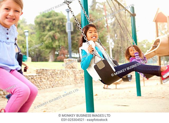 Three Young Girls Playing On Swing In Playground