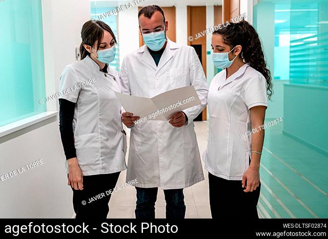 Doctor and nurses wearing protective face masks analyzing medical report in corridor at hospital