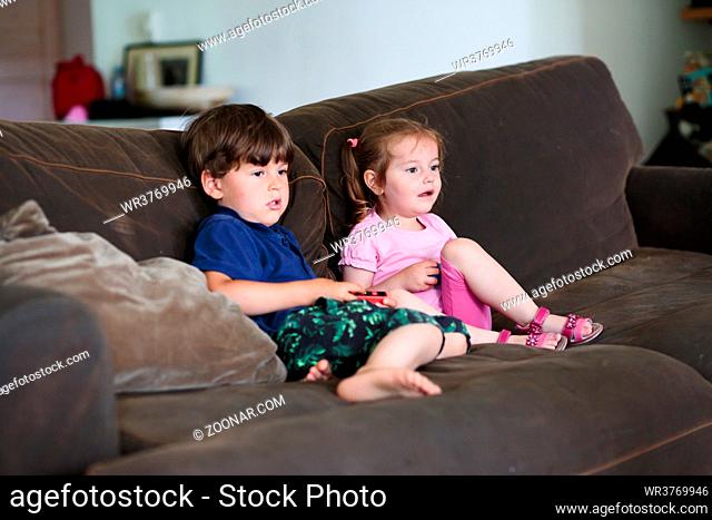 Concentrated toddlers boy and girl playing video game sitting on sofa at home