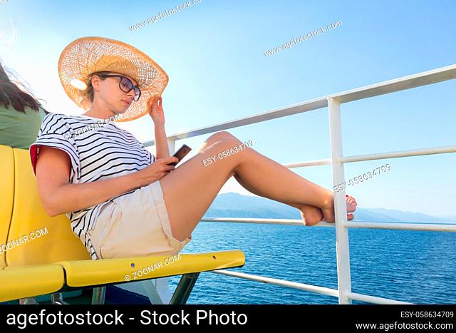Beautiful, romantic blonde woman on summer vacations traveling by cruse ship ferry boat holding and using mobile phone. Summer vacation lifestyle