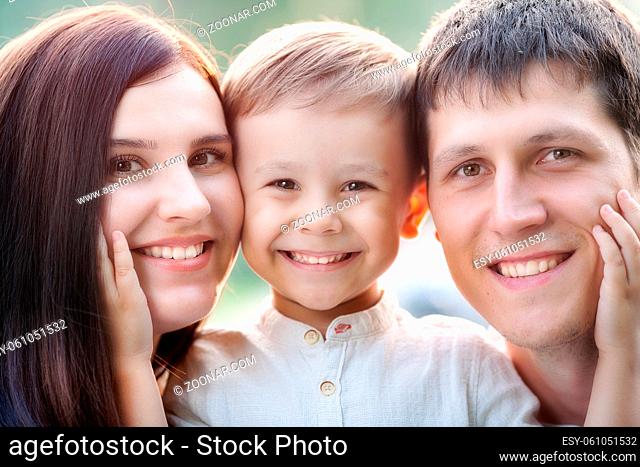 Close-up portrait of a happy young family. Mom, dad and little son look at the camera and smile. The faces of Caucasian parents and their child
