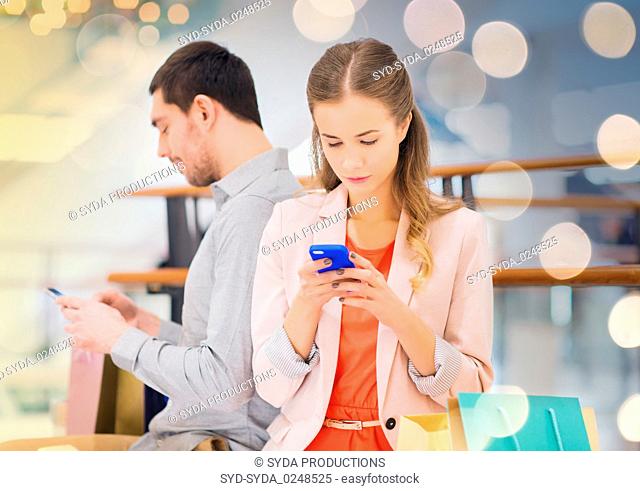 couple with smartphones and shopping bags in mall