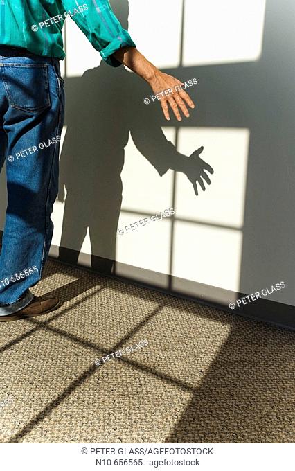Man standing by a wall and in the shadow coming from a nearby window