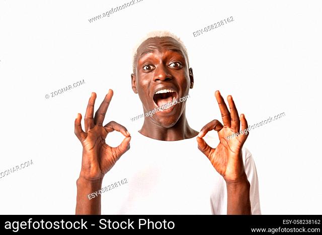 Close-up of excited attractive african-american blond guy express amazement, showing okay gesture in approval, standing white background