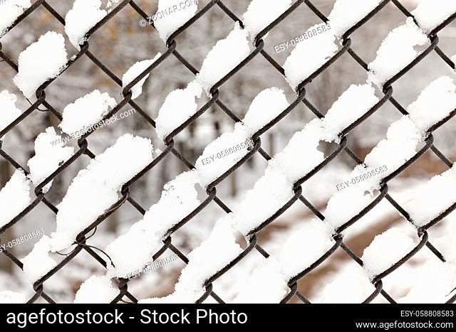 photo of a metal grating covered with white snow falling during a snowfall, close up