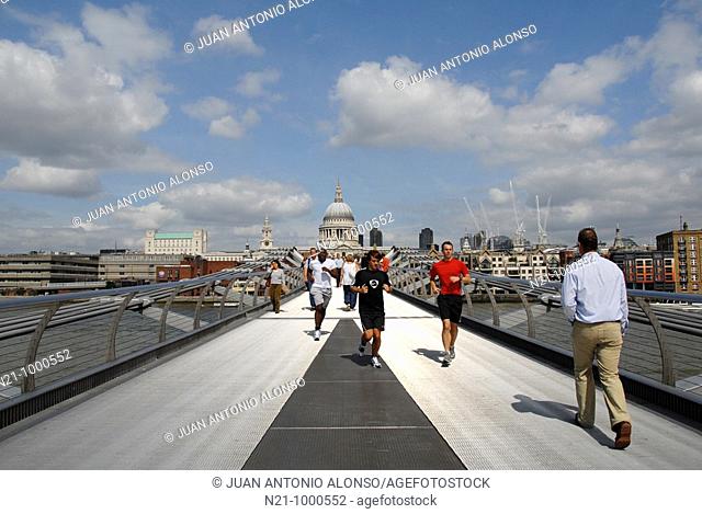 Pedestrians and joggers on Norman Foster’s Millenium Bridge over the river Thames. Saint Paul’s Cathedral is in the backlground