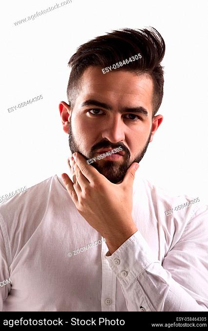 Portrait of doubtful handsome man looking at camera and touching his beard. Young hipster man posing for photographer isolated on white background