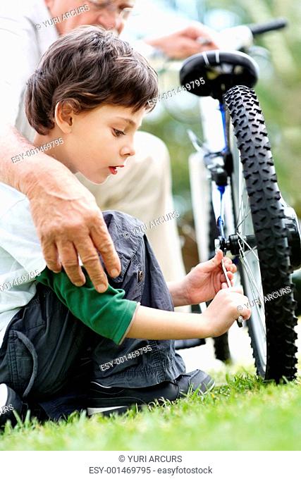 Portrait of little boy repairing a cycle tyre with grandfather - Outdoor