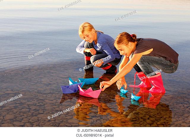 Two young girls floating paper boats on water