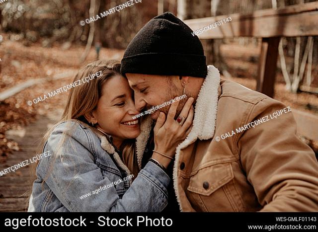Affectionate couple sitting on wooden bridge in forest