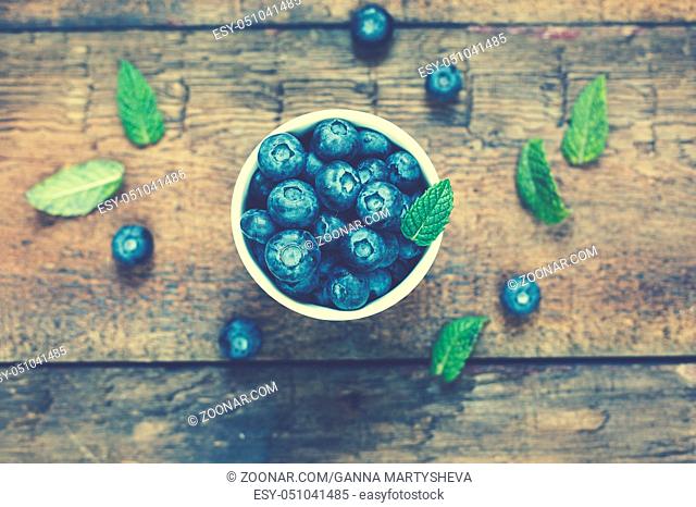 Blueberries in a white bowl and mint leaves on a wooden background, top view, rural style