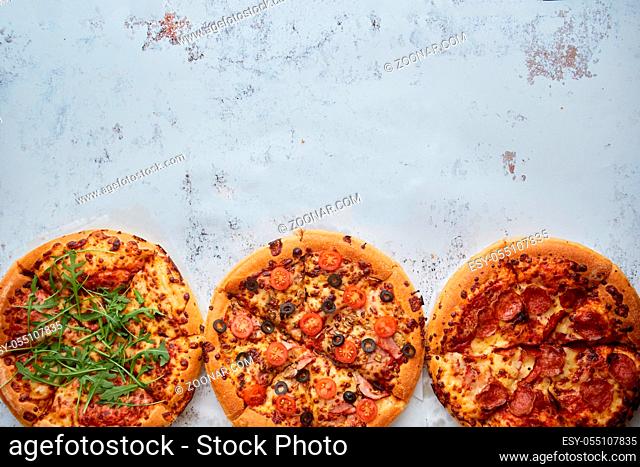 Three different kind of pizzas. Placed in a row on white rusty table. View from top with a space for your text