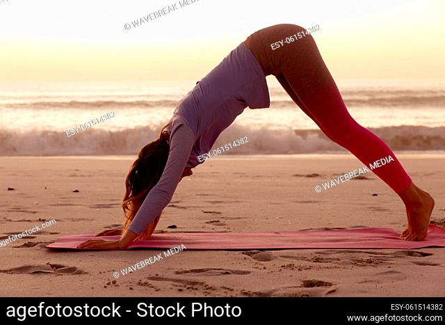 Woman performing yoga on the beach during sunset