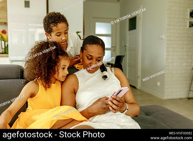 Woman sharing smart phone with children on sofa at home