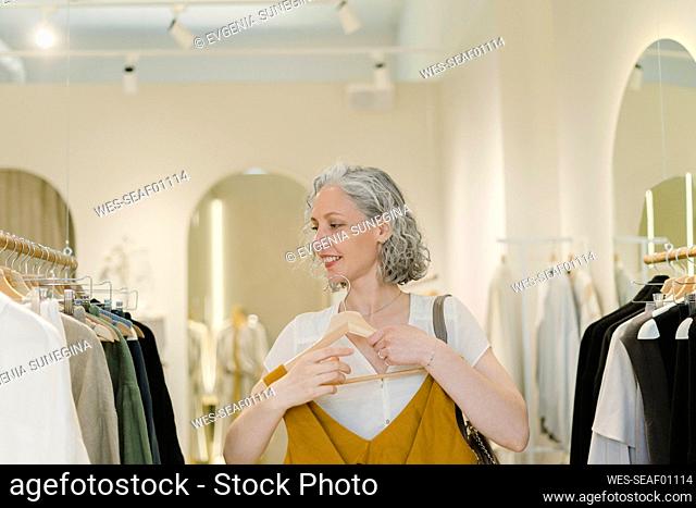 Smiling woman holding dress standing in clothes store