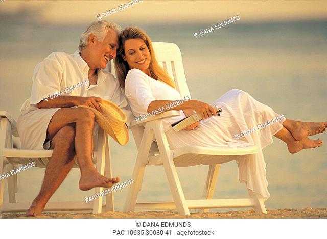 Senior man at the beach in chairs laughing with woman, couple relaxing