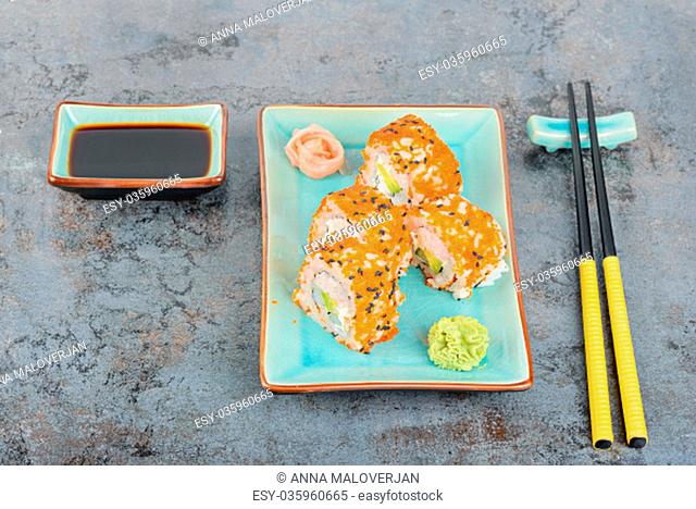 Sushi rolls with masago and soy sauce, served on turquoise plate and chopsticks over grey background. Top view