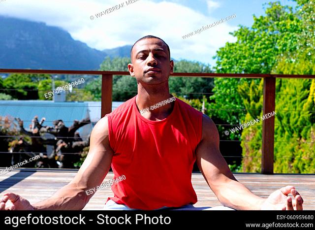 Young african american man meditating while practicing yoga at terrace on sunny day