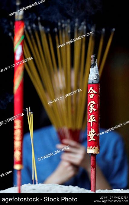 Ha Chuong Hoi Quan Pagoda.  Young Chinese woman praying with big burning incense sticks in her hand. Ho Chi Minh City. Vietnam