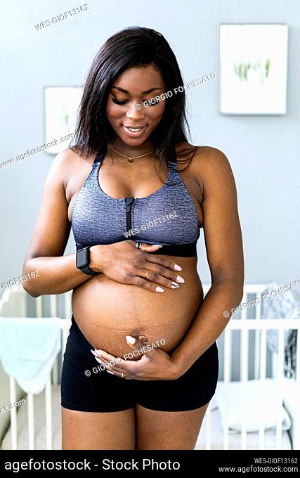 Smiling pregnant woman touching abdomen in bedroom