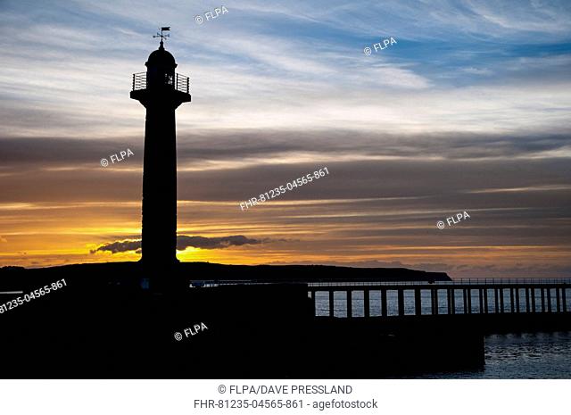 19th century stone lighthouse on pier, silhouetted at sunset, West Pier, Whitby, North Yorkshire, England, April