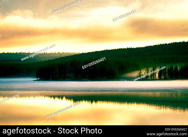 Misty calm evening on the forest lake is illuminated by the colors of sunset, melting ice, reflection in the water mirror. Spring in the Arctic North