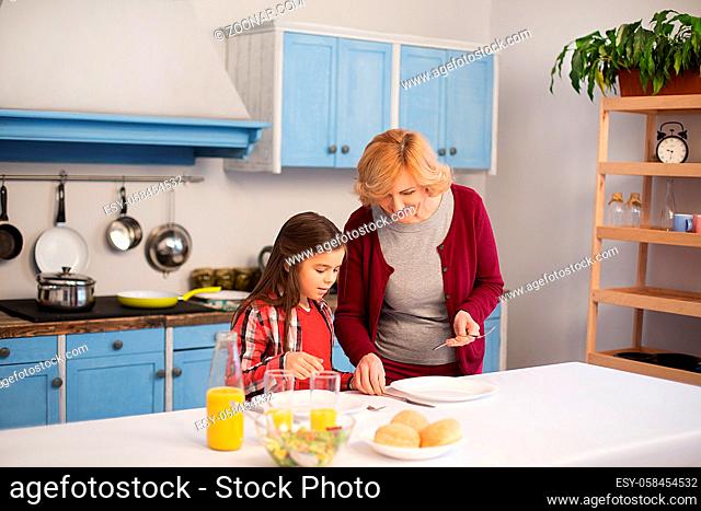 Granny shows little girl how to lay the table. Family dinner concept