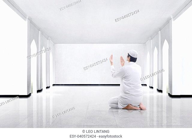 Back view of asian muslim man kneeling and praying to god in the mosque